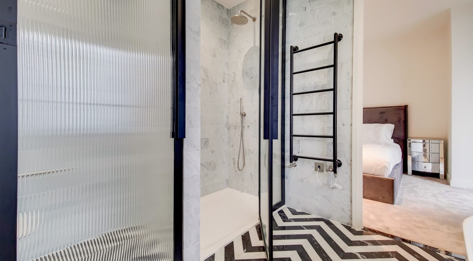 A finished en-suite shower room with marble tiling and chevron flooring, opening onto a bedroom